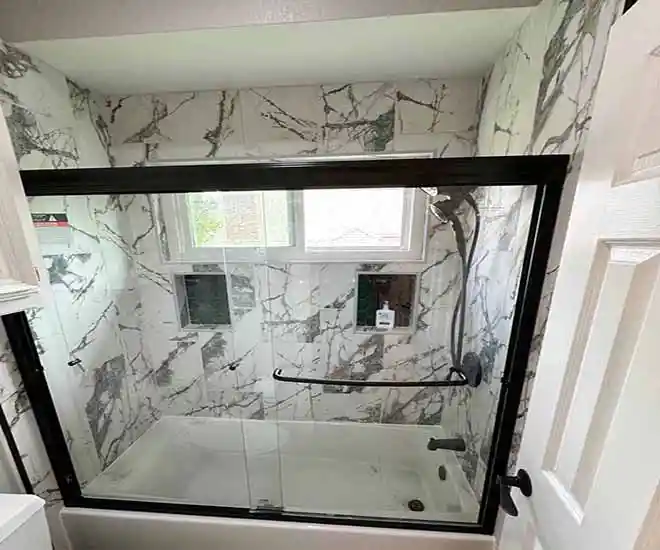 Bathroom after remodel featuring luxury marble‑style tile walls and black frame glass door